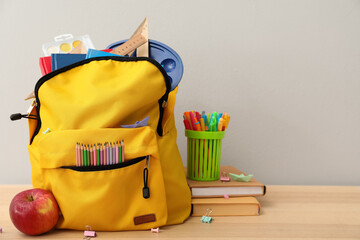 School backpack with stationery and apple on table against grey background - obrazy, fototapety, plakaty