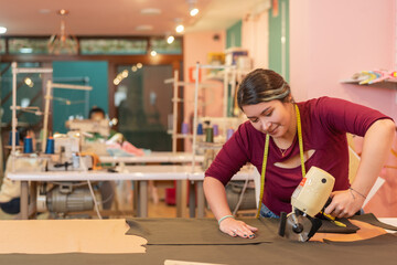 Woman cutting clothes with a power tool in a sewing shop