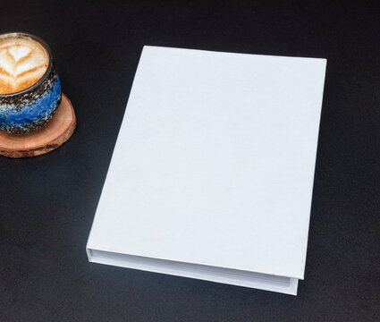 Mockup image of a blank white hardcover book on the top of a black table