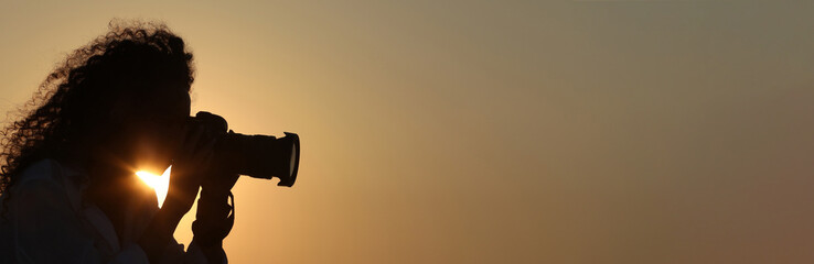 Photographer taking photo with professional camera outdoors at sunset, space for text. Banner design