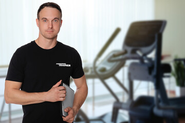 Fototapeta na wymiar Portrait of professional personal trainer with clipboard in gym. Space for text