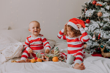 children in red and white pajamas eat Christmas sweets sitting in bed. boy and girl share gifts