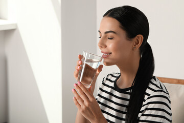 Young woman drinking water indoors, space for text. Refreshing drink