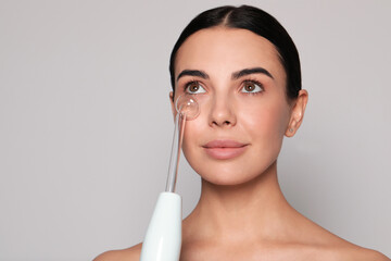 Woman using high frequency darsonval device on grey background. Space for text