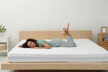 Happy young African American woman on bed with comfortable mattress at home
