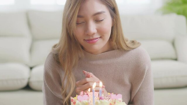 A young Asian woman is making a wish on her birthday before blowing out the candles on the cake. A woman sits on the floor and puts a cake on the table. Light a candle at home on her birthday.