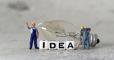 Light bulb and miniature people with business concept. White cube with the word 'IDEA'.

