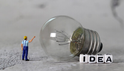 Light bulb and miniature people with business concept. White cube with the word 'IDEA'.

