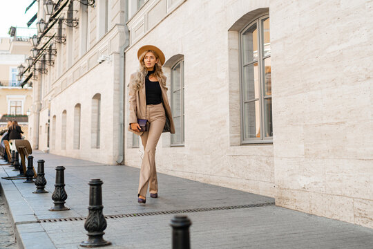Stunning blond woman in casual leather suit walking on the street in Paris. Outdoor fashion style. Beige hat and purse .  Full lenght.