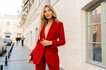 Beautiful smiling woman  in  elegant red velvet suit holding purse and  posin outdoor in old...