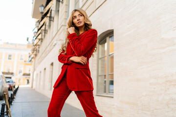 Profeshional fashion model in  elegant red velvet suit posin outdoor in old european city. - obrazy, fototapety, plakaty