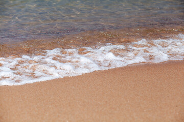 A soft wave runs on a sandy shore on a summer day. Empty space can be used as background for display or montage your top view products.