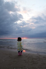 水平線に沈む夕日を見つめる小さな女の子の後ろ姿