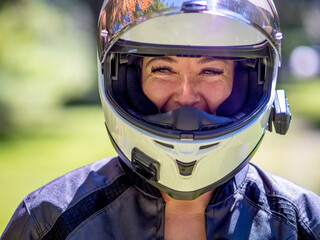 Young female motor cyclist wearing a full face helmet with visor open smiling