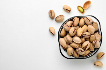 Bowl and pistachio nuts on white background, flat lay. Space for text