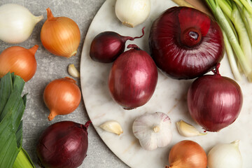 Fresh onion bulbs, leek and garlic on grey table, flat lay