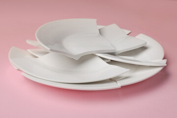 Pieces of broken ceramic plate on pink background, closeup
