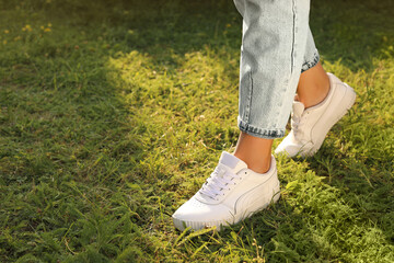 Woman in jeans and white shoes walking on green grass, closeup. Space for text