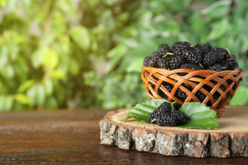 Fresh ripe black mulberries on wooden table against blurred background. Space for text