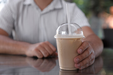 Man with plastic takeaway cup of delicious iced coffee at table in outdoor cafe, closeup. Space for...