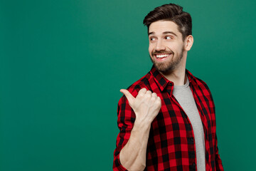 Side view young happy smiling man he 20s in red shirt grey t-shirt indicate point thumb finger aside on workspace area mock up isolated on plain dark green background studio People lifestyle concept