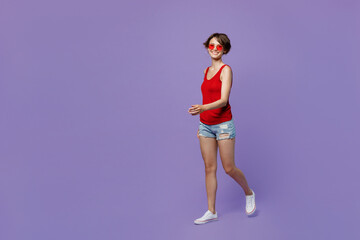 Fototapeta na wymiar Full body young smiling happy fun cheerful woman 20s she wear red tank shirt eyeglasses look camera walking goign strolling isolated on plain purple backround studio portrait People lifestyle concept