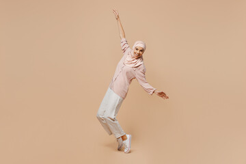 Fototapeta na wymiar Full body young arabian asian muslim woman she wear abaya hijab pink clothes stand on toes with outstretched hands leaning back dance isolated on plain beige background People islam religious concept