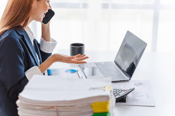 Young Attractive Asian business woman talking on mobile phone and working on laptop in modern office with financial reports.