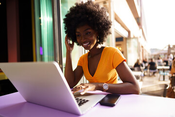 Obraz na płótnie Canvas Happy beautiful young black woman using laptop in cafe