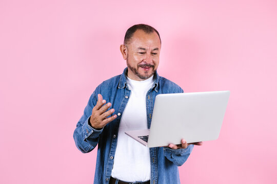 portrait of hispanic senior man wearing casual clothes and holding a computer on blue background in Mexico Latin America