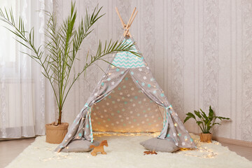 Cool children's wigwam in the room on the floor on white soft carpet with flowers near peetee tent. © sementsova321
