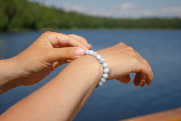 The girl straightens a beautiful bracelet on her hand on a sunny summer day against the backdrop of a lake and forest