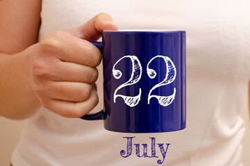 The inscription on the blue cup 22 july. Cup in female hand, business concept
