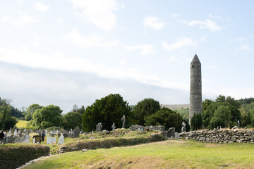 Fototapeta na wymiar A view of the round tower in the graveyard in the Glendalough monastery in Co Wicklow Ireland set in a valley on a sunny day showing perfectly green natural countryside. Irish tourist attraction