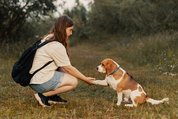 Teenage girl and dog in rural, side view. Young pet owner holding paw of dog