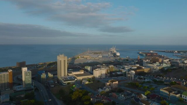 Forwards fly above coastal town at golden hour. Oversea harbour and large ships. Port Elisabeth, South Africa