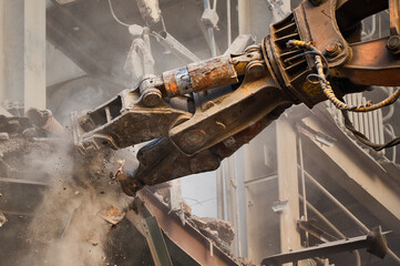 Hydraulic scissors on rigging demolish industrial building