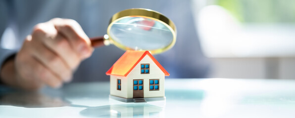 Businessman Holding Magnifying Glass Over House Model