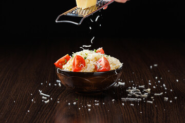 Chef's hands grate parmesan cheese on pasta with cheese and tomatoes. Traditional Italian food.