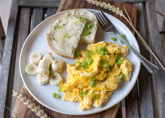 Breakfast plate with scrambled eggs, buttered white bread and bananas