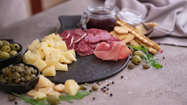 making meat and cheese antipasto plater - woman putting pieces of prosciutto ham on stone serving board at domestic kitchen