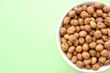 Chufa, tigernut, earth almond on ceramic bowl on green background with copy space for text. Healthy organic food concept. Tiger nut for flour, milk, traditional typical drink horchata Valencia Spain