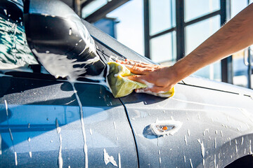 A man washes his car with foam at a self-service car wash, close-up