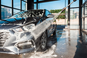 Self-service car wash. A man washes off the foam from his car with water from a pressurized hose at...