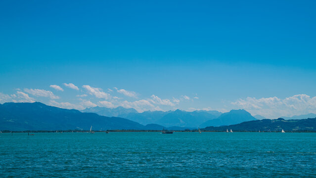 Germany, Bodensee panorama landscape view to austria nature mountains and alps from water with many sailboats in summer with sun