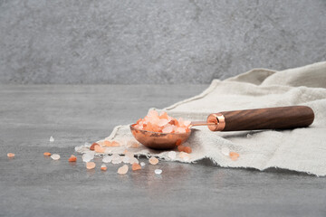 Himalayan pink salt in a spoon and cloth on stone background
