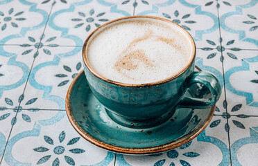Cappuccino or latte with frothy foam, blue coffee cup on tile background. Cafe and bar concept.