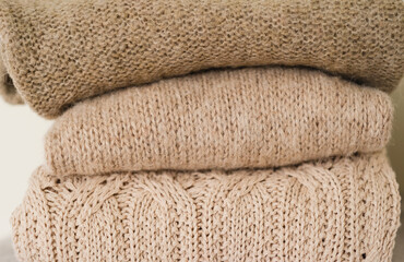 closeup knitted textures of beige wool sweaters. stack of cozy autumn and winter knitwear