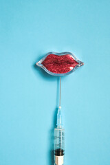 Lips and injection syringe with hyaluronic acid on a blue background. Lip augmentation concept. Flat lay, vertical image.