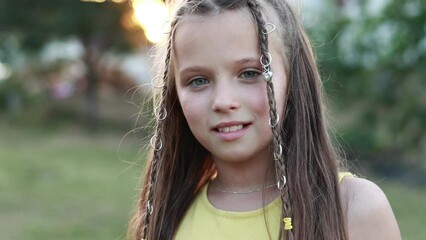 front view of adorable little girl with hairstyle is smiling with her outdoors on summer day. caucasian friendly and shy kid looking at camera posing. Happy childhood on holiday vacation.
